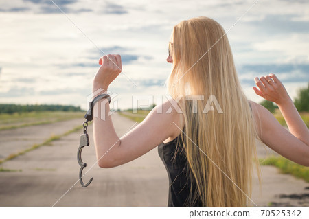 A beautiful married model girl with long hair with handcuffs on her hands is walking along an empty road to meet freedom. Family Violence	 70525342