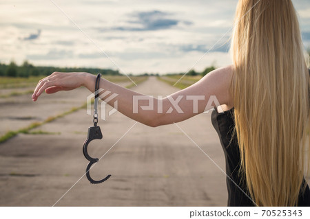 A beautiful married model girl with long hair with handcuffs on her hands is walking along an empty road to meet freedom. Family Violence	 70525343