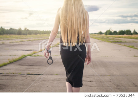 A beautiful married model girl with long hair with handcuffs on her hands is walking along an empty road to meet freedom. Family Violence A beautiful married model girl with long hair with handcuffs on her hands is walking along an empty road to meet freedom. Family Violence 70525344