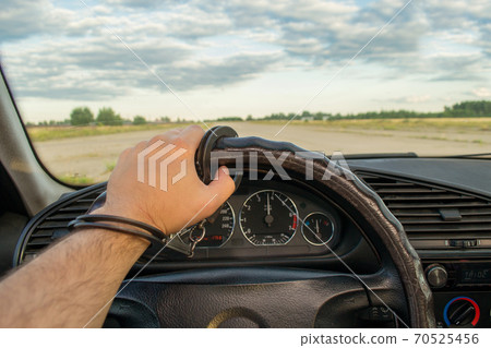 The man's hand is handcuffed to the steering wheel of the car against the background of a flying airplane The man's hand is handcuffed to the steering wheel of the car against the background of a flying airplane 70525456