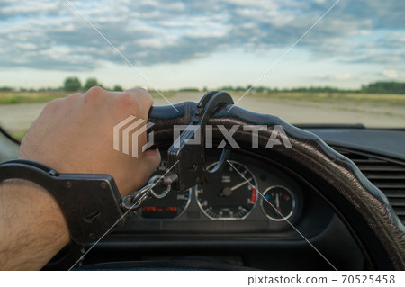 The man's hand is handcuffed to the steering wheel of the car against the background of a flying airplane The man's hand is handcuffed to the steering wheel of the car against the background of a flying airplane 70525458