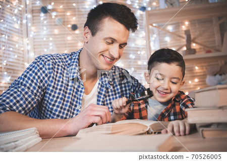 Father and son are reading book with magnifier. Father and son are reading book with magnifier. 70526005