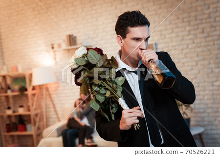 Man with flowers stands at home and drinks alcohol Man with flowers stands at home and drinks alcohol 70526221