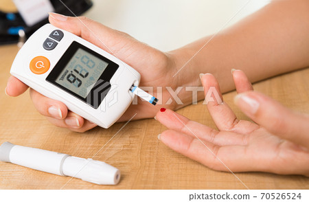 World diabetes day concept. Close up hands holding lancing device with blood to checking blood sugar level by Glucose meter for diabetes tester. World diabetes day concept. Close up hands holding lancing device with blood to checking blood sugar level by Glucose meter for diabetes tester. 70526524