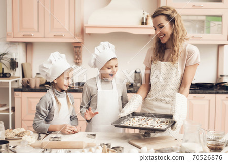 Children in chef hats with mother in kitchen.  70526876
