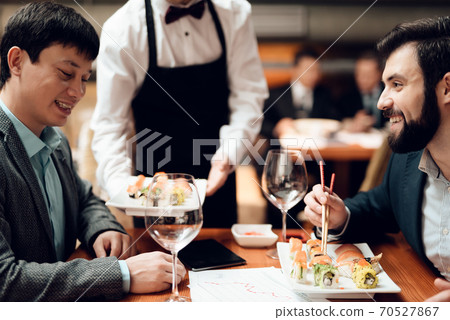 Two businessmen sit at a table and eat sushi. Two businessmen sit at a table and eat sushi. 70527867