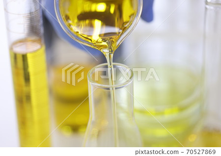 Scientist's hand in rubber glove pours yellow liquid into glass test tube in chemical laboratory closeup 70527869