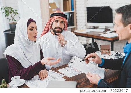 Arab couple sits at a table with a realtor. Arab couple sits at a table with a realtor. 70528647