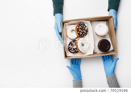 Waiter gives order during coronavirus epidemic and fast customer service. Client takes box of donuts with white and chocolate glazed and crumb and two cups of coffee takeaway 70529166