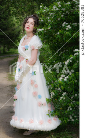 Young woman in an long white bride dress in flowers tree 70529383