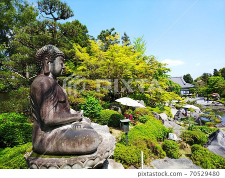 佛教寺廟花園和池塘，岩石和新鮮的綠樹，後面右前方的石佛後面 70529480