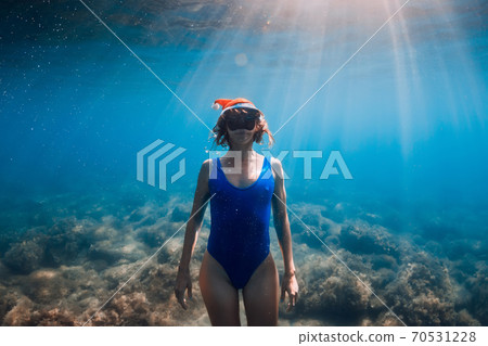 Happy freediver woman with Christmas cap posing underwater in blue ocean. Christmas holidays concept Happy freediver woman with Christmas cap posing underwater in blue ocean. Christmas holidays concept 70531228