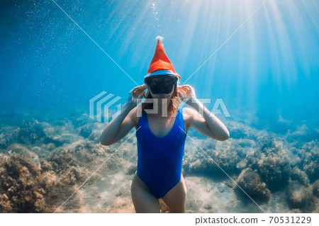 Happy freediver woman with Christmas cap posing underwater in blue ocean. Christmas holidays concept Happy freediver woman with Christmas cap posing underwater in blue ocean. Christmas holidays concept 70531229