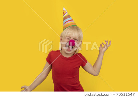 Little kid with party hat and red nose clown having fun. Portrait on yellow background. Party for children 70531547