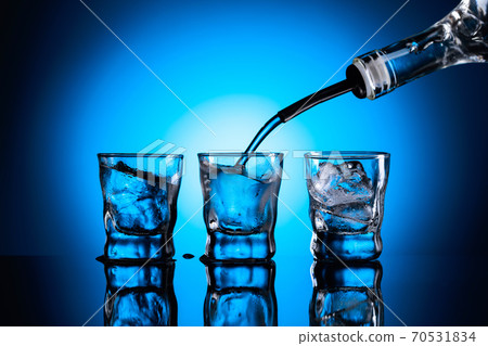 Vodka is poured from bottle into glasses with ice. 70531834