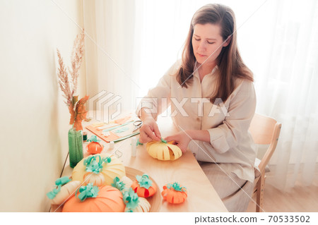 A young woman sits at a desk and makes a homemade paper pumpkin A young woman sits at a desk and makes a homemade paper pumpkin 70533502