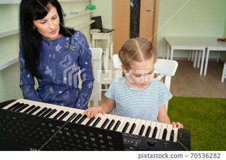 teacher teaches little girl to play on keyboard. teacher teaches little girl to play on keyboard. 70536282