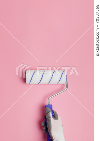 Paint roller in gloved hand on pink background Paint roller in gloved hand on pink background 70537368