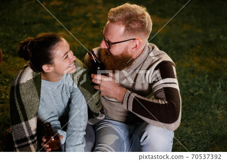 Friends having fun on the night picnic with drinks. Young caucasian couple at bbq in countryside Friends having fun on the night picnic with drinks. Young caucasian couple at bbq in countryside 70537392