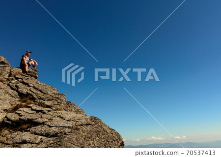 A man stands on the edge of a stone on one of the peaks of the Ukrainian Carpathians, the Montenegrin ridge, picturesque mountains on the trampled trails of the Carpathians. A man stands on the edge of a stone on one of the peaks of the Ukrainian Carpathians, the Montenegrin ridge, picturesque mountains on the trampled trails of the Carpathians. 70537413