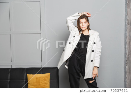Young elegant woman in white oversize blazer and black ripped pants. Interior portrait Young elegant woman in white oversize blazer and black ripped pants. Interior portrait 70537451