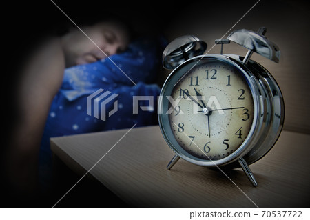 a man sleeping on the bed beside the alarm clock on table, in night. 70537722