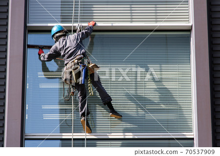 Man washes glass on high-rise building. Service cleaning the windows on the house. Man washes glass on high-rise building. Service cleaning the windows on the house. 70537909