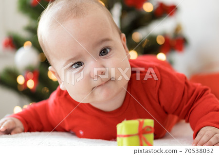 merry christmas christmas and happy new year, infants, childhood, holidays concept - close-up 6 month old newborn baby in red clothers on his tummy crawls with decorations gifts near christmas tree. 70538032