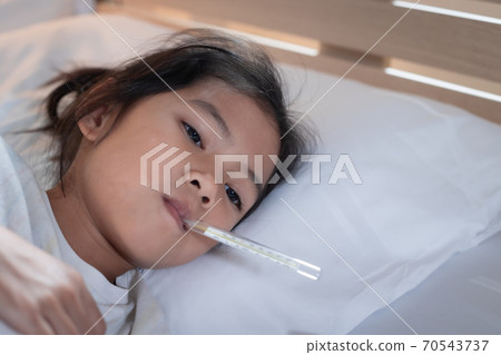 Sick asian child girl is sleeping on bed and measuring her body temperature with thermometer in the bedroom at home. Sick asian child girl is sleeping on bed and measuring her body temperature with thermometer in the bedroom at home. 70543737