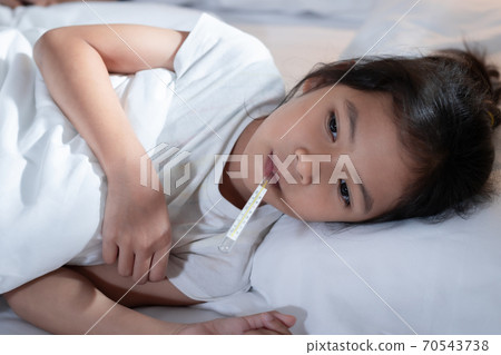 Sick asian child girl is sleeping on bed and measuring her body temperature with thermometer in the bedroom at home. Sick asian child girl is sleeping on bed and measuring her body temperature with thermometer in the bedroom at home. 70543738