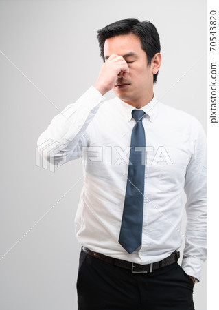 Exhausted Asian worker Squeezing between the eyebrows to try relaxing from hard work shows pain expression face, concept working exhausted, office worker lifestyle, office syndrome, tiring work hour. 70543820