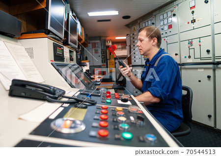 Marine engineer officer controlling vessel engines and propulsion in engine control room 70544513