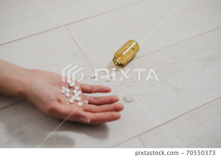 Close-up of a hand with a handful of pills in the palm, lying lifeless on the floor. Nearby is a bottle of pills. The consequences of depression, suicide. 70550373
