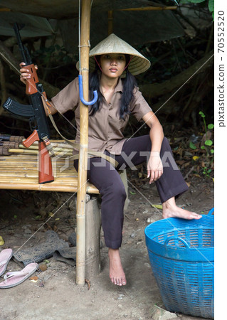 A young woman with a submachine gun under a bamboo shelter 70552520