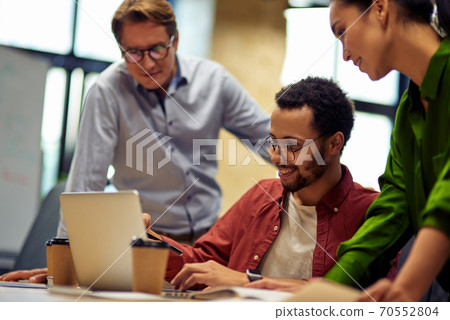 Group of focused multiracial business people looking at laptop screen and discussing work or project results while standing in the modern office or coworking space Group of focused multiracial business people looking at laptop screen and discussing work or project results while standing in the modern office or coworking space 70552804