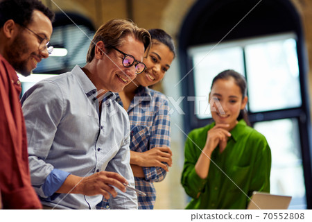Positive male boss discussing project results and sharing ideas with young motivated multi ethnic team while standing together in the modern office Positive male boss discussing project results and sharing ideas with young motivated multi ethnic team while standing together in the modern office 70552808