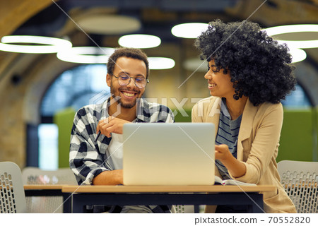 Two young happy multiracial business people sitting at the desk in the modern office, using laptop and discussing project, man and woman working together in coworking space Two young happy multiracial business people sitting at the desk in the modern office, using laptop and discussing project, man and woman working together in coworking space 70552820