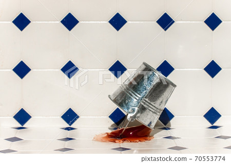 A metal bucket falls to the floor and splashes out the colored liquid. 70553774