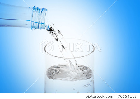 Pouring water from plastic bottle into glass on white background. 70554115