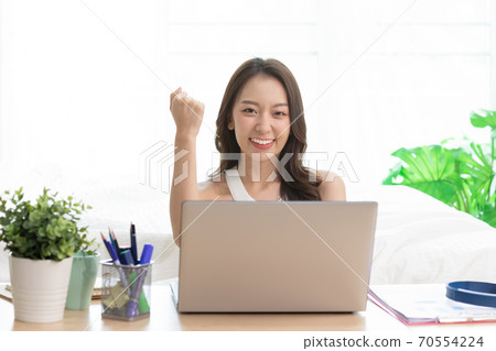 Asian woman working on a laptop sitting on the bed in the house. 70554224