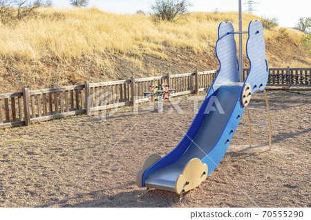Metallic and wooden slide with other swings in a children's playground with gravel Metallic and wooden slide with other swings in a children's playground with gravel 70555290