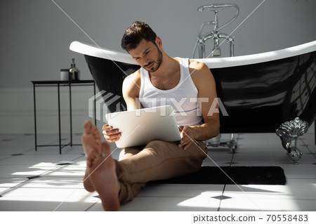 Man with laptop sitting near bath 70558483
