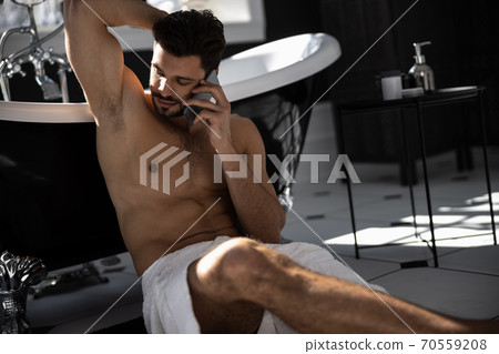 Handsome man wrapped in towel talking on mobile phone and sitting on floor 70559208
