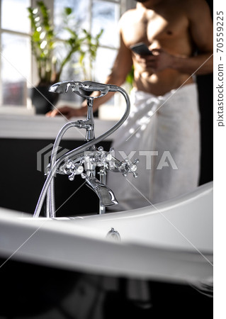 Cropped sjot of man wrapped in towel showing mobile phone ain bathroom 70559225