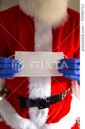 Man wearing santa claus costume holding safety mask and wearing protective gloves for Coronavirus, Covid-19 and Christmas concept Man wearing santa claus costume holding safety mask and wearing protective gloves for Coronavirus, Covid-19 and Christmas concept 70560752