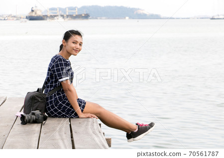 young woman with camera sitting on a wooden pier over the sea. young woman with camera sitting on a wooden pier over the sea. 70561787