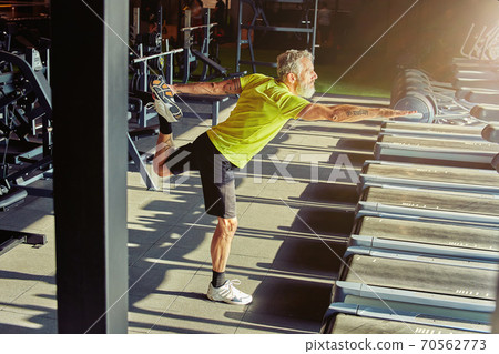 Warming up exercises. Full length shot of a mature athletic man in sportswear doing stretching exercises before workout in a gym Warming up exercises. Full length shot of a mature athletic man in sportswear doing stretching exercises before workout in a gym 70562773