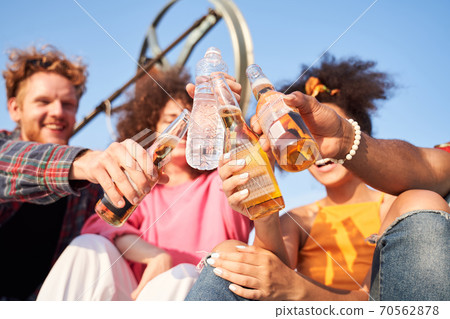 Happy friends clinking bottles of beverages outdoors Happy friends clinking bottles of beverages outdoors 70562878