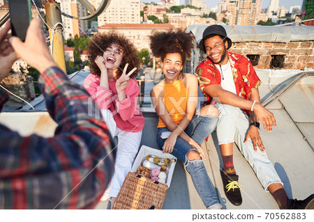 Guy taking photo of jolly friends on urban roof 70562883