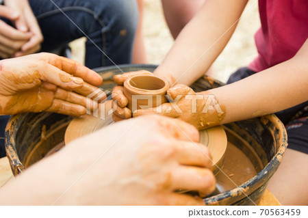A close up view on ceramic production process on potter's wheel with children. Clay crafts with kids concept A close up view on ceramic production process on potter's wheel with children. Clay crafts with kids concept 70563459